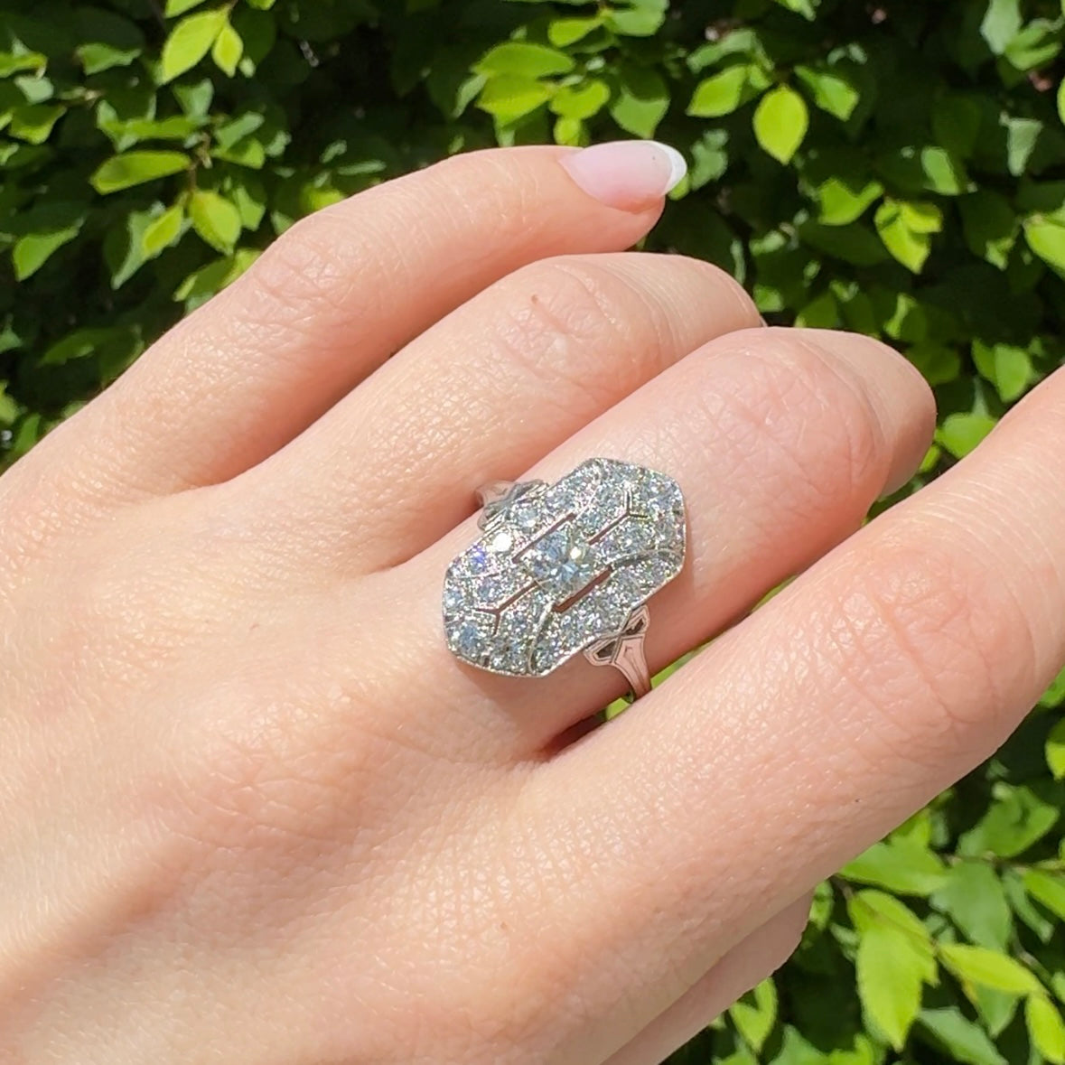 Art Deco Tiffany platinum and diamond navette shaped ring on hand behind green leaves