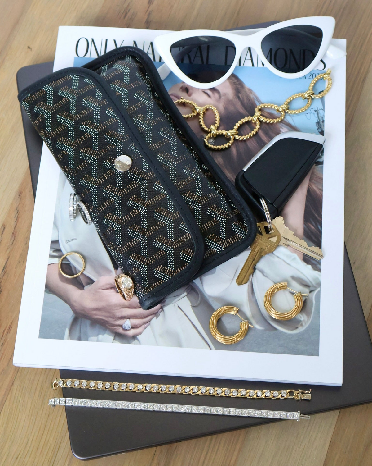 Black patterned wallet on top of a magazine with sunglasses and jewelry images.