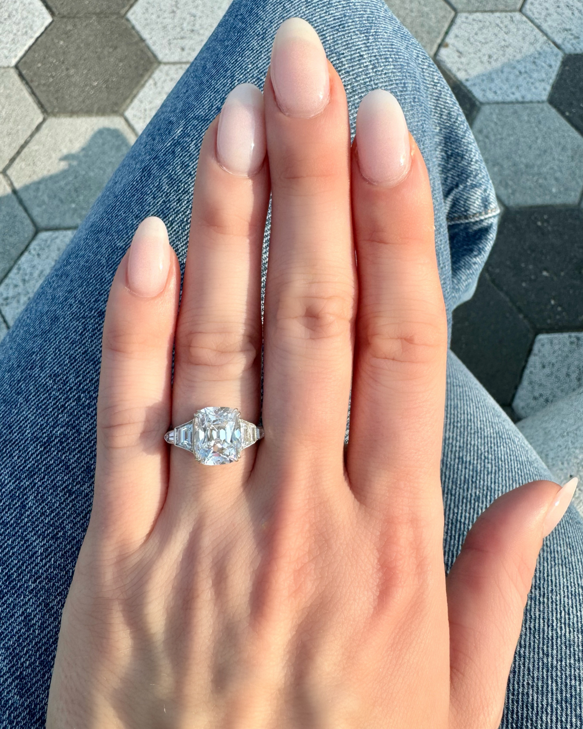 Hand wearing a diamond ring on a hexagonal tile floor