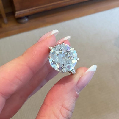 Round diamond engagement ring on a hand with a neutral background