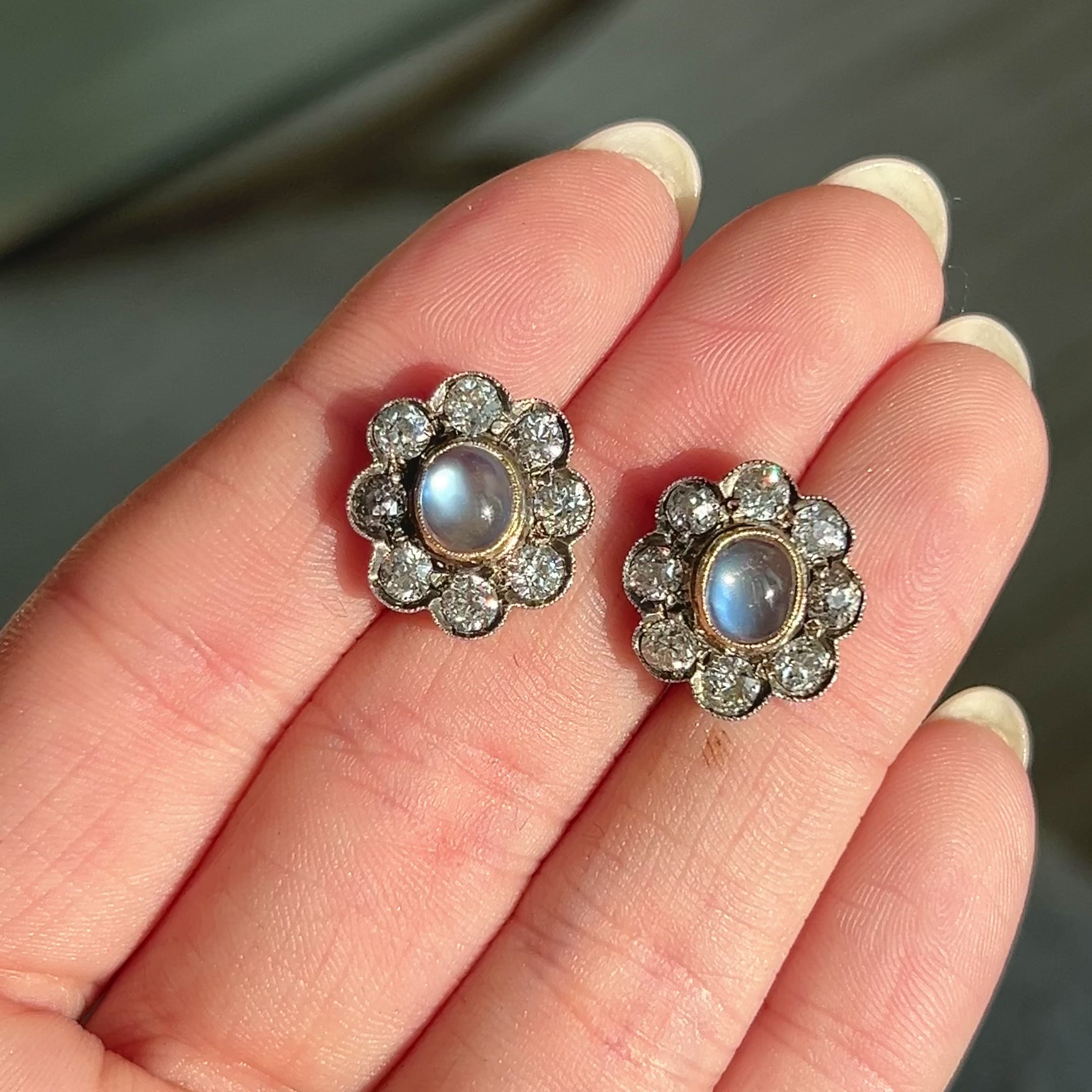 Antique earrings featuring lively bezel-set moonstones, with old mine-cut diamonds in a halo surround, set in silver topped gold. Video of earrings in hand.