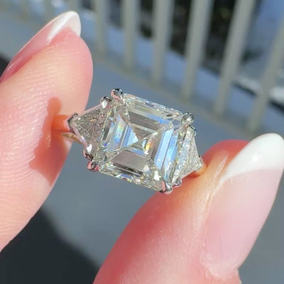 Emerald cut diamond engagement ring on a hand with a neutral background