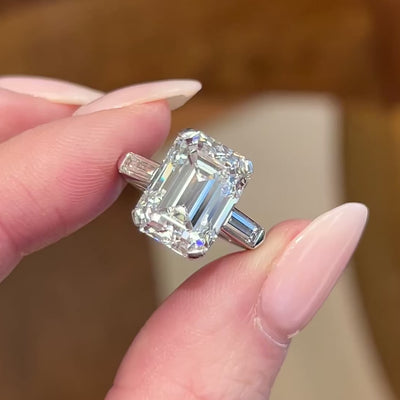 Emerald cut diamond engagement ring on a hand with a neutral background