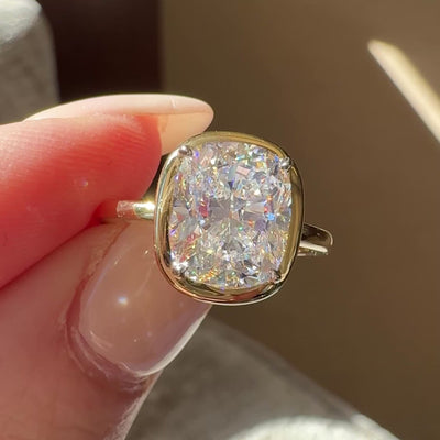 Bezel set cushion diamond engagement ring on a hand with a neutral background